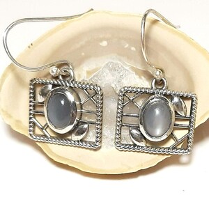 May include: Silver dangle earrings with a gray moonstone set in a silver cage design.