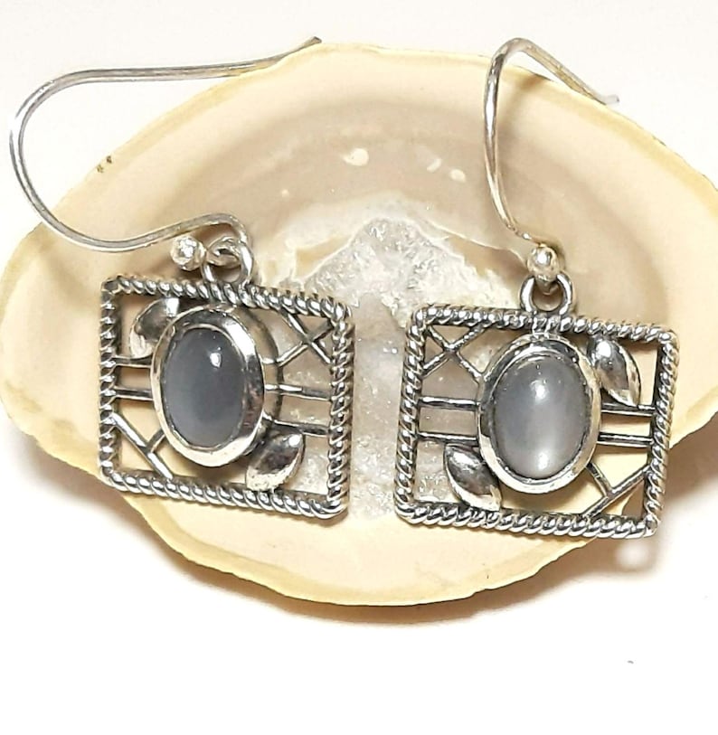 May include: Silver dangle earrings with a gray moonstone set in a silver cage design.