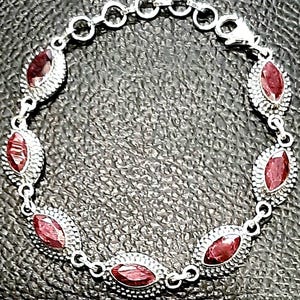 May include: A silver bracelet with red gemstone accents. The bracelet has a chain link design and features oval-shaped gemstones.