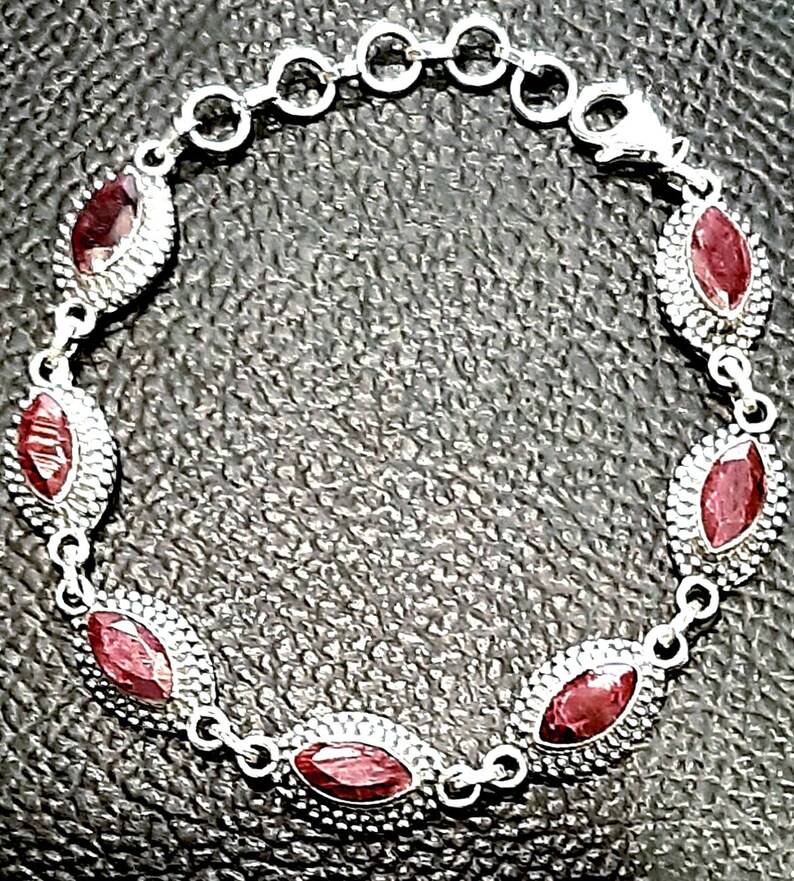 May include: A silver bracelet with red gemstone accents. The bracelet has a chain link design and features oval-shaped gemstones.