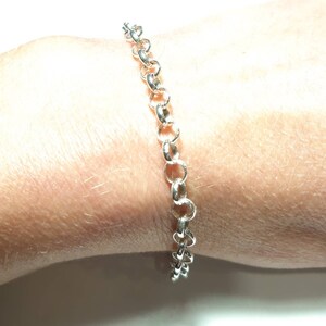 Puede incluir: Un brazalete de cadena de plata con un dise&ntilde;o delicado y enlazado. El brazalete se muestra en la mu&ntilde;eca de una persona.