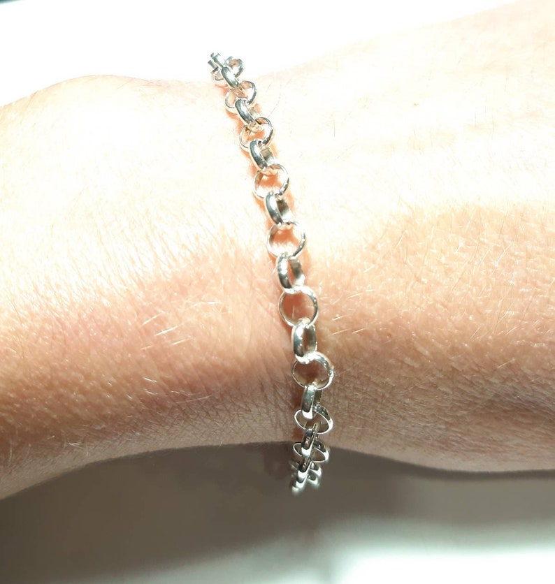 Puede incluir: Un brazalete de cadena de plata con un dise&ntilde;o delicado y enlazado. El brazalete se muestra en la mu&ntilde;eca de una persona.