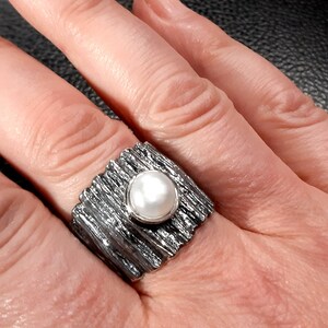 May include: A silver ring with a textured band and a white pearl in the center.