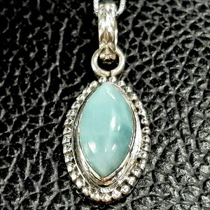 May include: A silver pendant necklace with a light blue oval-shaped gemstone set in a silver bezel. The pendant has a detailed silver design around the gemstone.