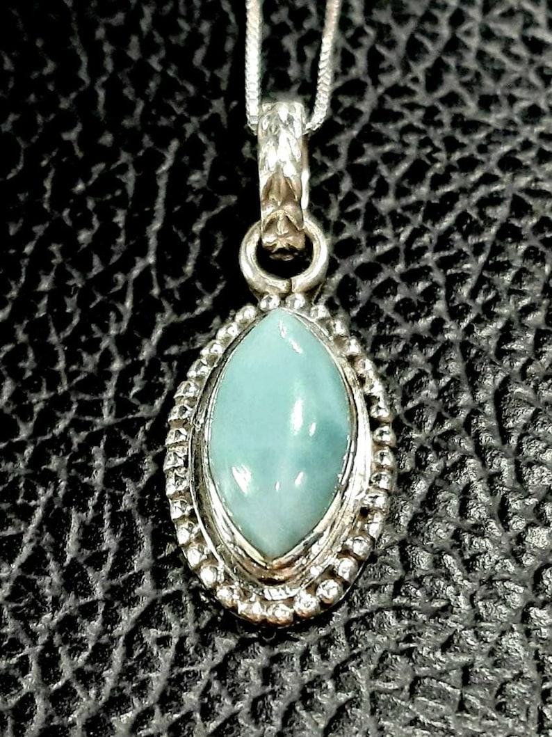 May include: A silver pendant necklace with a light blue oval-shaped gemstone set in a silver bezel. The pendant has a detailed silver design around the gemstone.