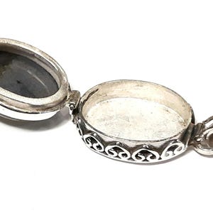 Peut inclure: Collier avec m&eacute;daillon en argent avec un pendentif de forme ovale. Le m&eacute;daillon est ouvert, r&eacute;v&eacute;lant un int&eacute;rieur vide. Le m&eacute;daillon a une bordure d&eacute;corative avec un motif floral.