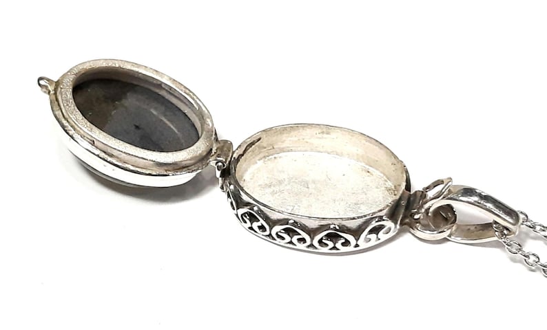 Peut inclure: Collier avec m&eacute;daillon en argent avec un pendentif de forme ovale. Le m&eacute;daillon est ouvert, r&eacute;v&eacute;lant un int&eacute;rieur vide. Le m&eacute;daillon a une bordure d&eacute;corative avec un motif floral.