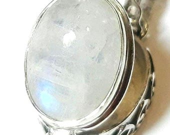 May include: An oval-shaped pendant featuring a smooth, translucent white moonstone cabochon set in a polished silver frame. The base of the pendant displays intricate, openwork scroll patterns in silver, and it hangs from a delicate silver chain.
