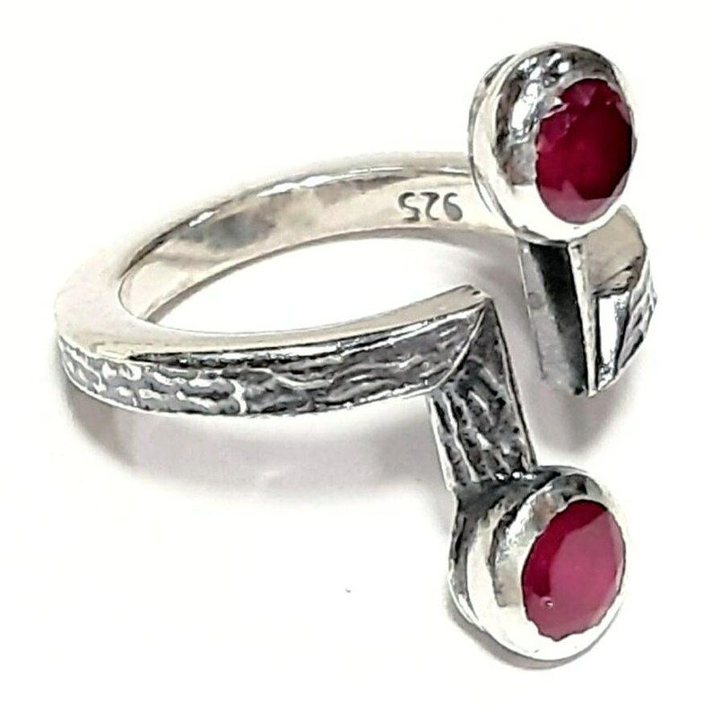 Op de afbeelding: Een zilveren ring met twee rode robijnstenen die in de band zijn gezet. De ring is getextureerd en heeft een uniek ontwerp.