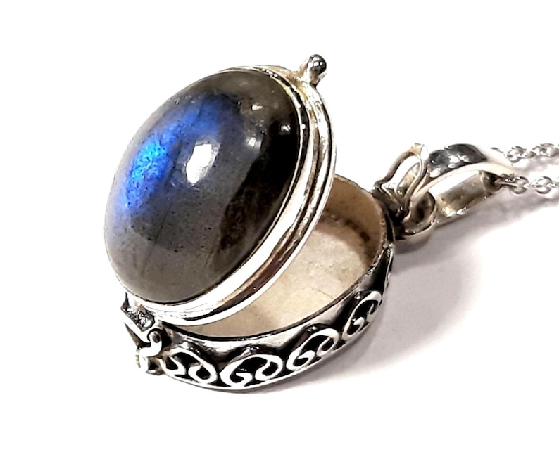Peut inclure: Un collier avec un pendentif en argent en forme de m&eacute;daillon orn&eacute; d'une pierre de labradorite bleue. Le m&eacute;daillon est ouvert, r&eacute;v&eacute;lant un petit compartiment &agrave; l'int&eacute;rieur.