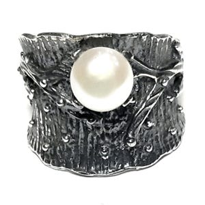 May include: A silver ring with a textured, organic design featuring a large white pearl in the center.