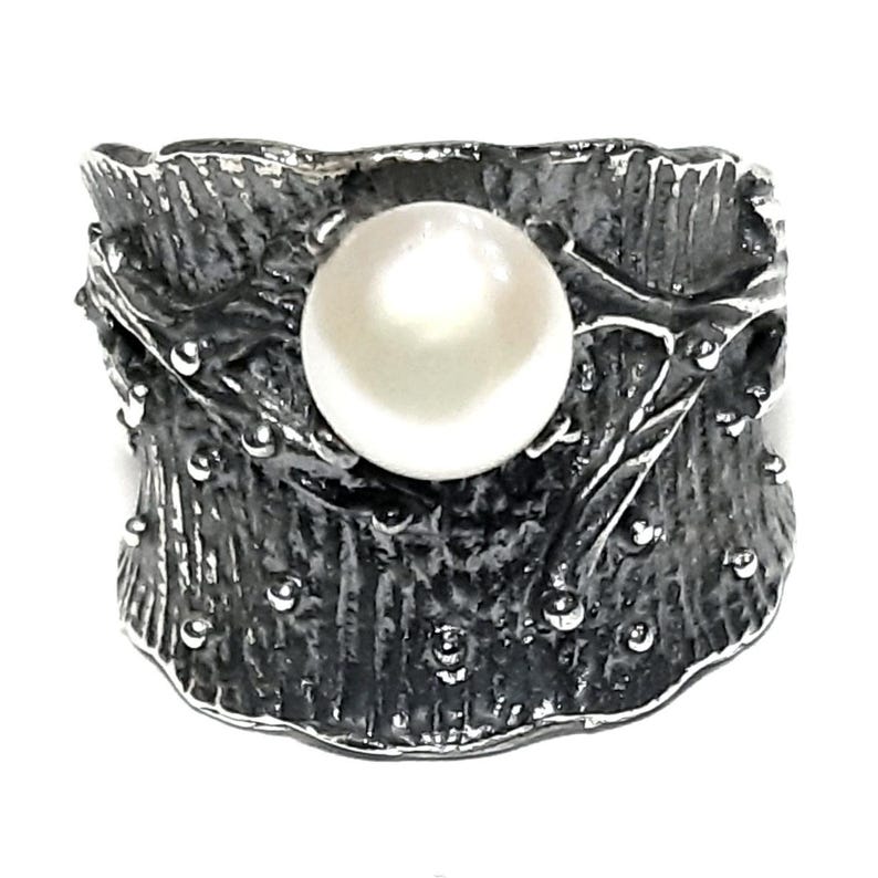 May include: A silver ring with a textured, organic design featuring a large white pearl in the center.