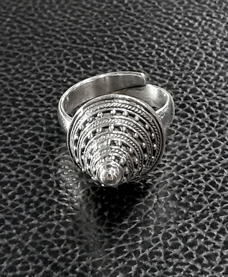 May include: A silver ring with a cone-shaped design. The cone is made up of multiple layers of intricate detailing, including small beads and lines.