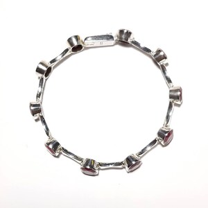 May include: A silver bracelet with red gemstones. The bracelet has a clasp closure.