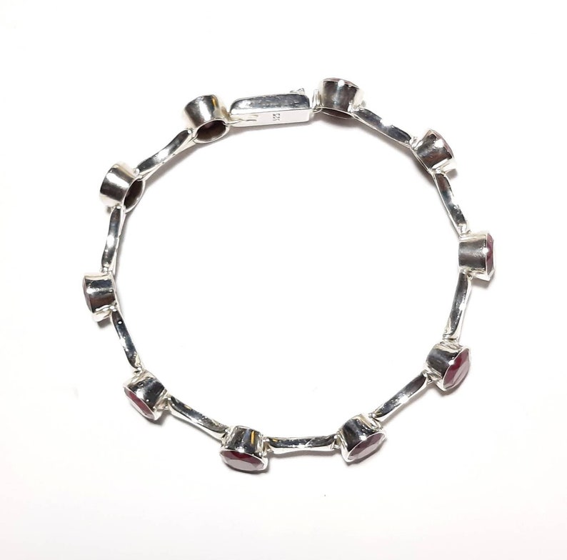May include: A silver bracelet with red gemstones. The bracelet has a clasp closure.