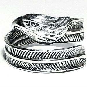 May include: A silver-toned ring featuring an eagle head design. The ring wraps around the finger with a feather motif. The eagle's head is detailed with textured feathers and a focused eye, creating a striking, nature-inspired accessory.