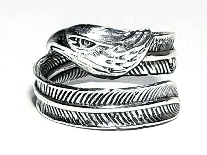 May include: A silver-toned ring featuring an eagle head design. The ring wraps around the finger with a feather motif. The eagle's head is detailed with textured feathers and a focused eye, creating a striking, nature-inspired accessory.