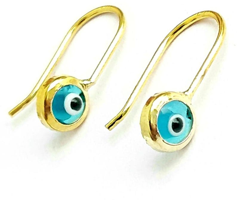 K&ouml;nnte beinhalten: Ein Paar goldene Ohrringe mit einem blauen b&ouml;sen Blick-Anh&auml;nger. Die Ohrringe sind aus Gold gefertigt und haben ein schlichtes Design. Der b&ouml;se Blick-Anh&auml;nger ist ein beliebtes Symbol f&uuml;r Schutz und Gl&uuml;ck.