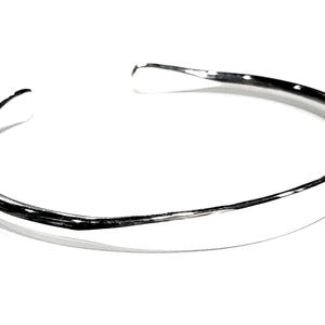 May include: A silver bangle bracelet with a smooth, rounded surface.