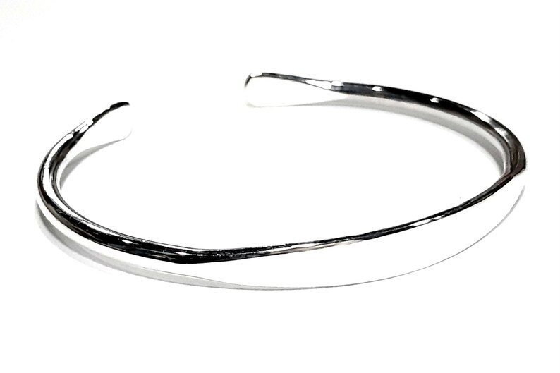 May include: A silver bangle bracelet with a smooth, rounded surface.