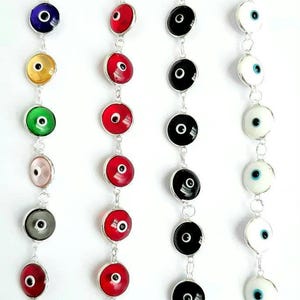 May include: A set of nine silver chain bracelets with round, colorful evil eye charms. The charms are red, blue, yellow, green, pink, gray, black, and white.
