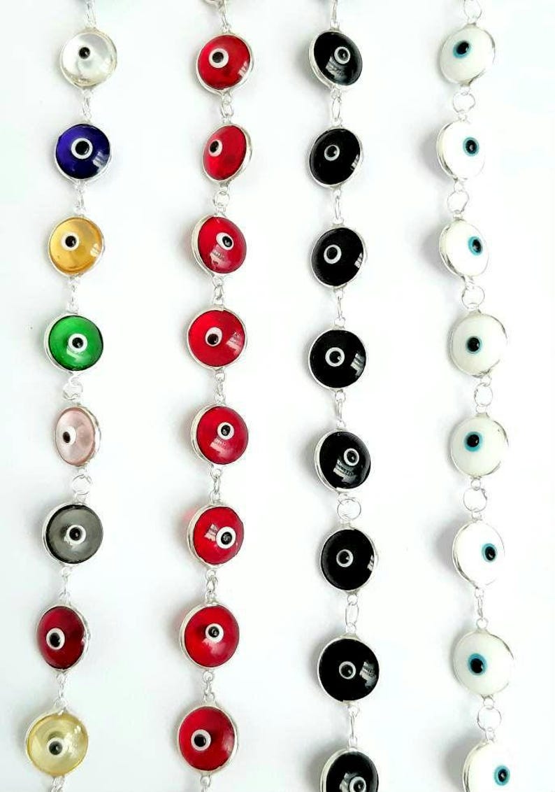May include: A set of nine silver chain bracelets with round, colorful evil eye charms. The charms are red, blue, yellow, green, pink, gray, black, and white.