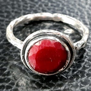 Pu&ograve; includere: Un anello d'argento con una pietra preziosa rossa incastonata in una montatura a castone. La fascia dell'anello &egrave; testurizzata e ha una finitura martellata.