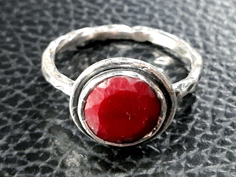 Pu&ograve; includere: Un anello d'argento con una pietra preziosa rossa incastonata in una montatura a castone. La fascia dell'anello &egrave; testurizzata e ha una finitura martellata.