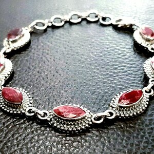 May include: A silver bracelet with red gemstone accents. The bracelet features a chain link design and oval-shaped gemstones set in silver.