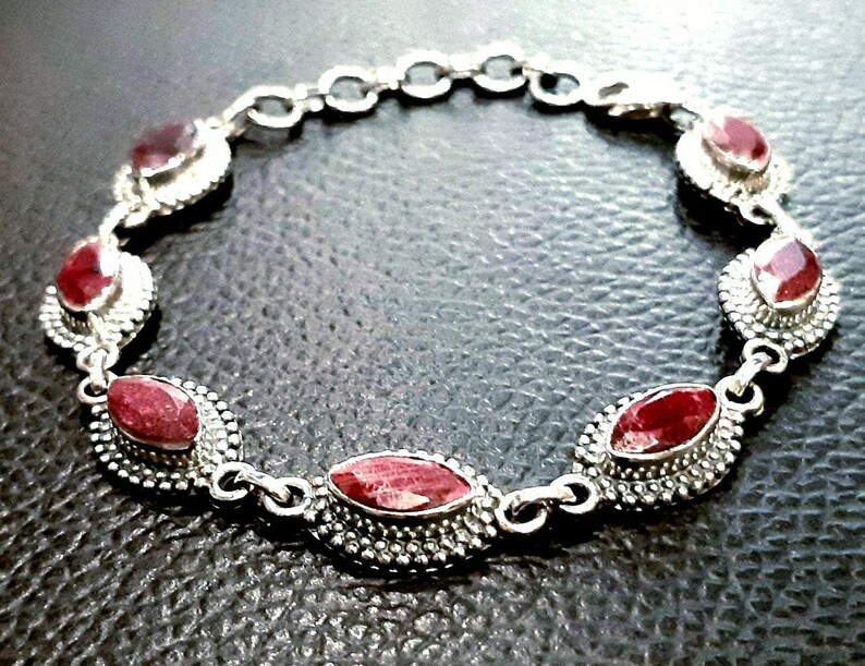 May include: A silver bracelet with red gemstone accents. The bracelet features a chain link design and oval-shaped gemstones set in silver.