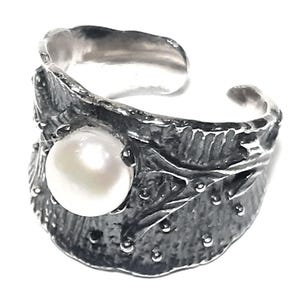 May include: A silver ring with a large white pearl set in a textured, leaf-shaped design.