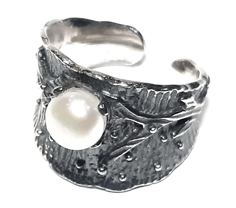 May include: A silver ring with a large white pearl set in a textured, leaf-shaped design.