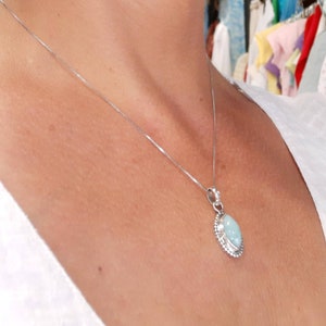 May include: A silver chain necklace with a light blue oval pendant. The pendant has a silver border and a smooth, polished surface.