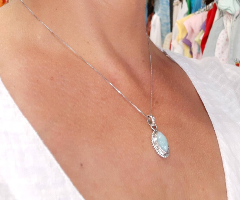 May include: A silver chain necklace with a light blue oval pendant. The pendant has a silver border and a smooth, polished surface.