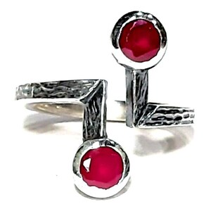 Op de afbeelding: Een zilveren ring met twee rode edelstenen. De ring heeft een getextureerde, gehamerde afwerking en een uniek, asymmetrisch ontwerp.