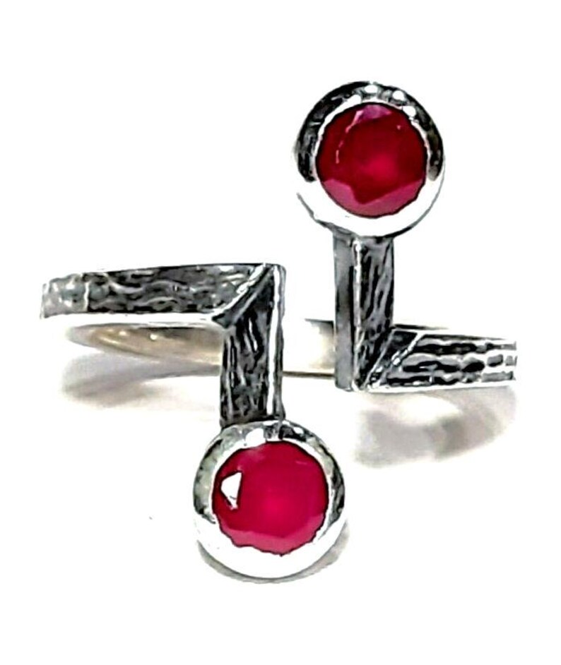 Op de afbeelding: Een zilveren ring met twee rode edelstenen. De ring heeft een getextureerde, gehamerde afwerking en een uniek, asymmetrisch ontwerp.
