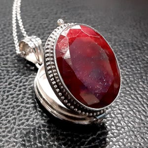 May include: A silver locket necklace featuring a large, oval-shaped, red gemstone. The locket is open, revealing a blank interior.