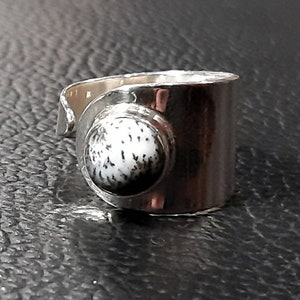 May include: A silver ring with a white and black stone set in the center. The ring is wide and has a simple design.