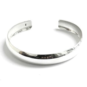 May include: A silver bangle bracelet with a smooth, rounded surface.