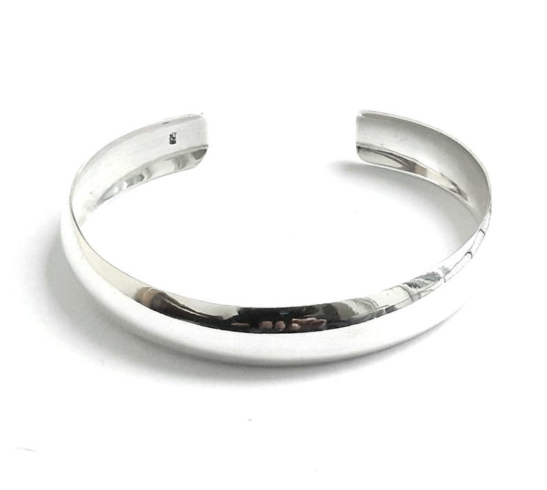 May include: A silver bangle bracelet with a smooth, rounded surface.