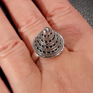 May include: A silver ring with a cone-shaped design. The cone is made up of multiple layers of intricate silverwork, with small beads around the edges.