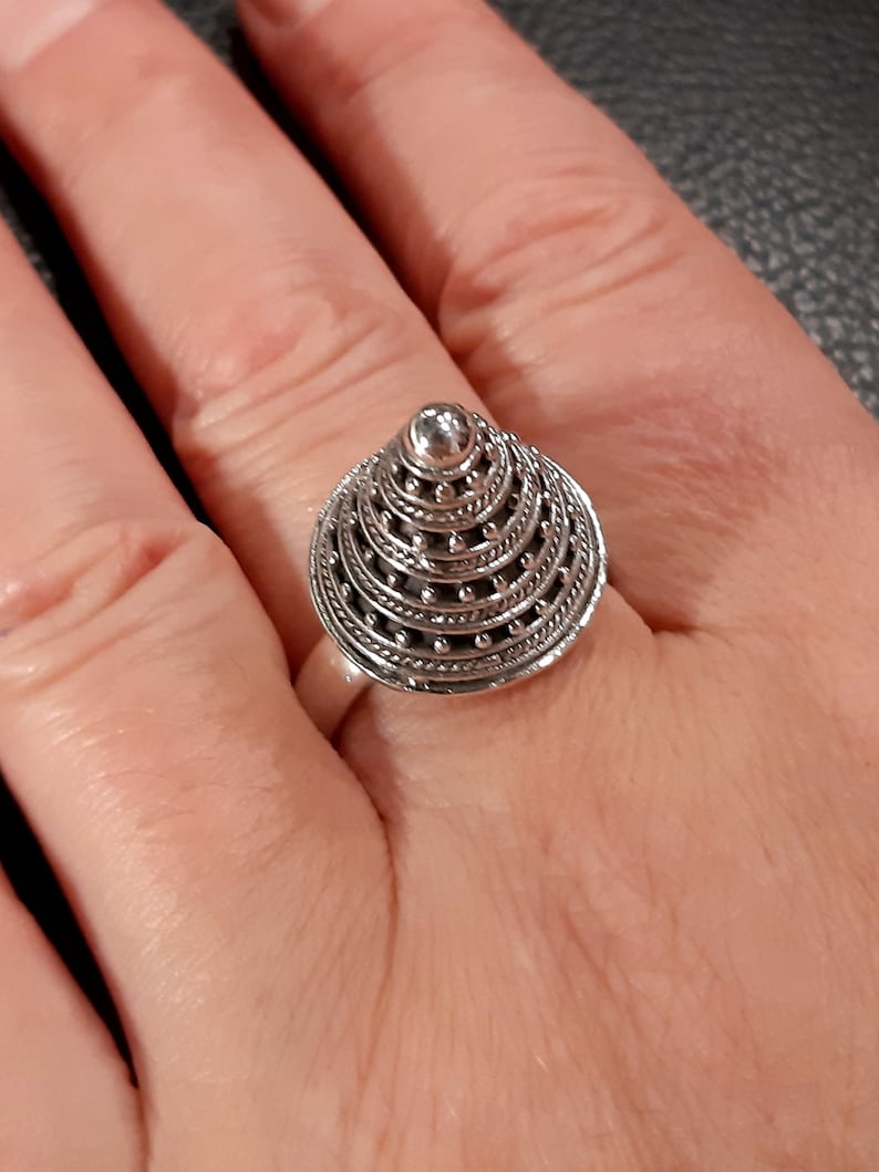 May include: A silver ring with a cone-shaped design. The cone is made up of multiple layers of intricate silverwork, with small beads around the edges.