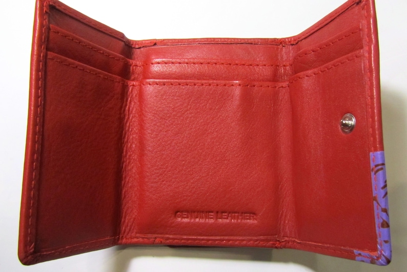 May include: Red leather trifold wallet with a snap closure and the words "Genuine Leather" embossed on the inside.