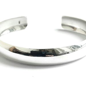 May include: A silver bangle bracelet with a smooth, rounded surface.