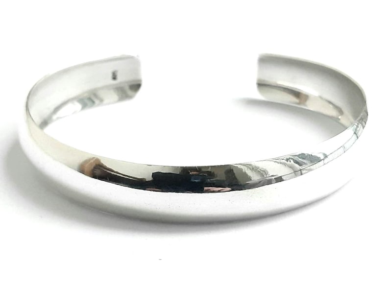 May include: A silver bangle bracelet with a smooth, rounded surface.
