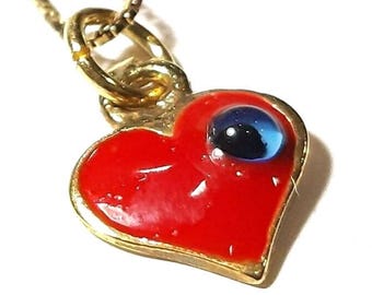 May include: A gold chain necklace with a red heart pendant featuring a blue evil eye charm.