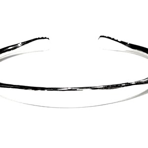 May include: A silver bangle bracelet with a smooth, rounded surface.