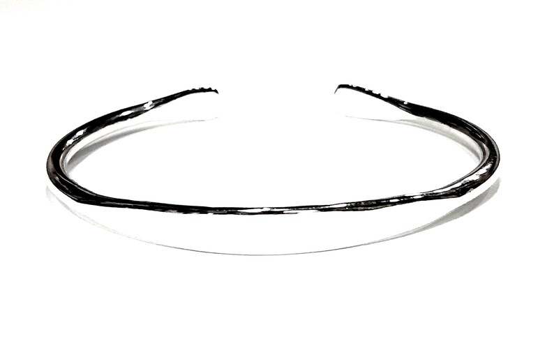 May include: A silver bangle bracelet with a smooth, rounded surface.