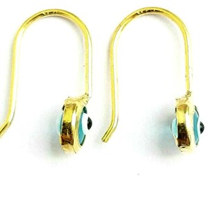 K&ouml;nnte beinhalten: Ein Paar goldene Ohrringe mit einem blauen b&ouml;sen Augen-Anh&auml;nger. Die Ohrringe sind aus Gold und haben einen Hakenverschluss.