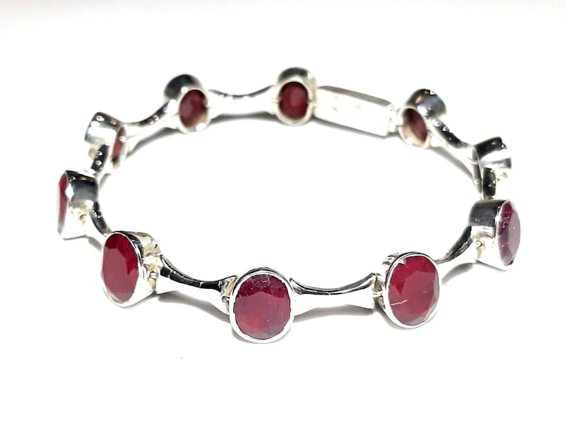 May include: A silver bangle bracelet with red gemstones. The bracelet is made of a series of connected silver links, each with a red gemstone set in the center.